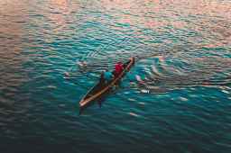 three people on brown canoe sailing on calm water